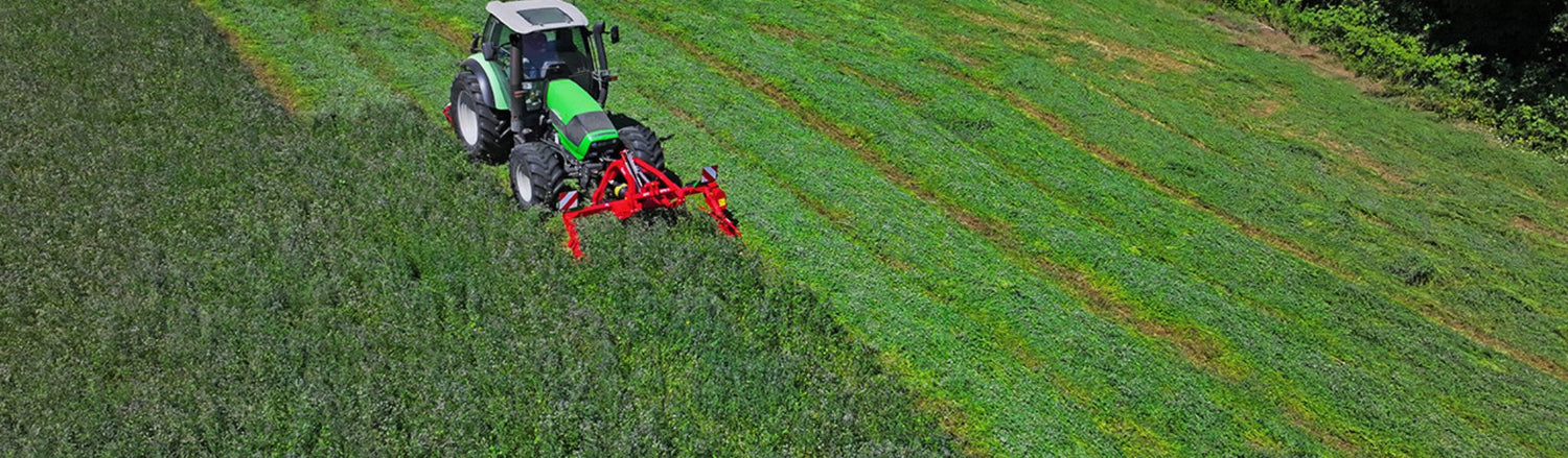 Traktor med röd slåtterbalk i arbete på grön vallåker – professionell slåtter för lantbruk