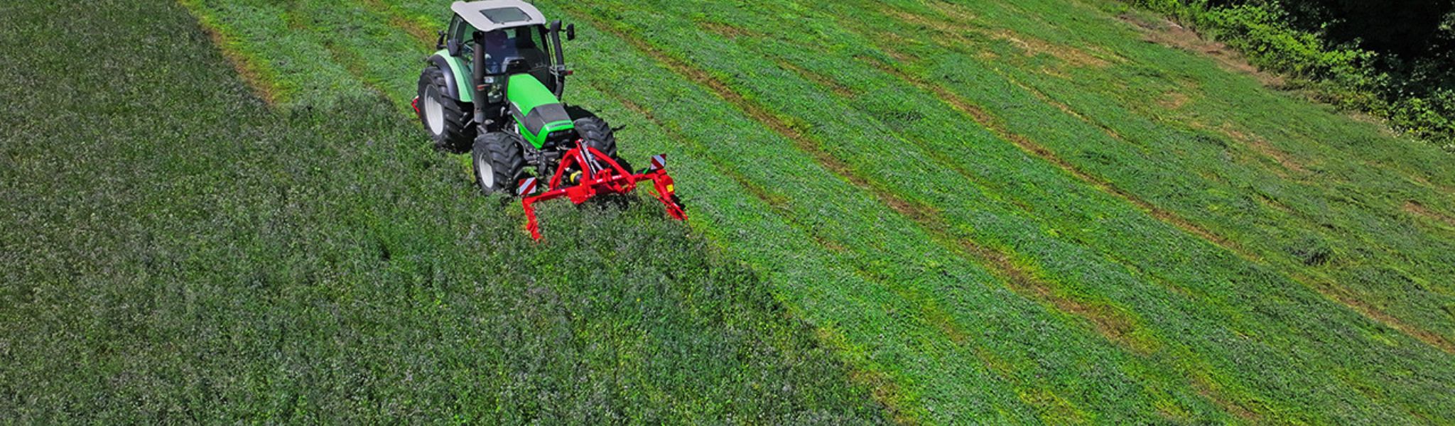 Traktor med röd slåtterbalk i arbete på grön vallåker – professionell slåtter för lantbruk