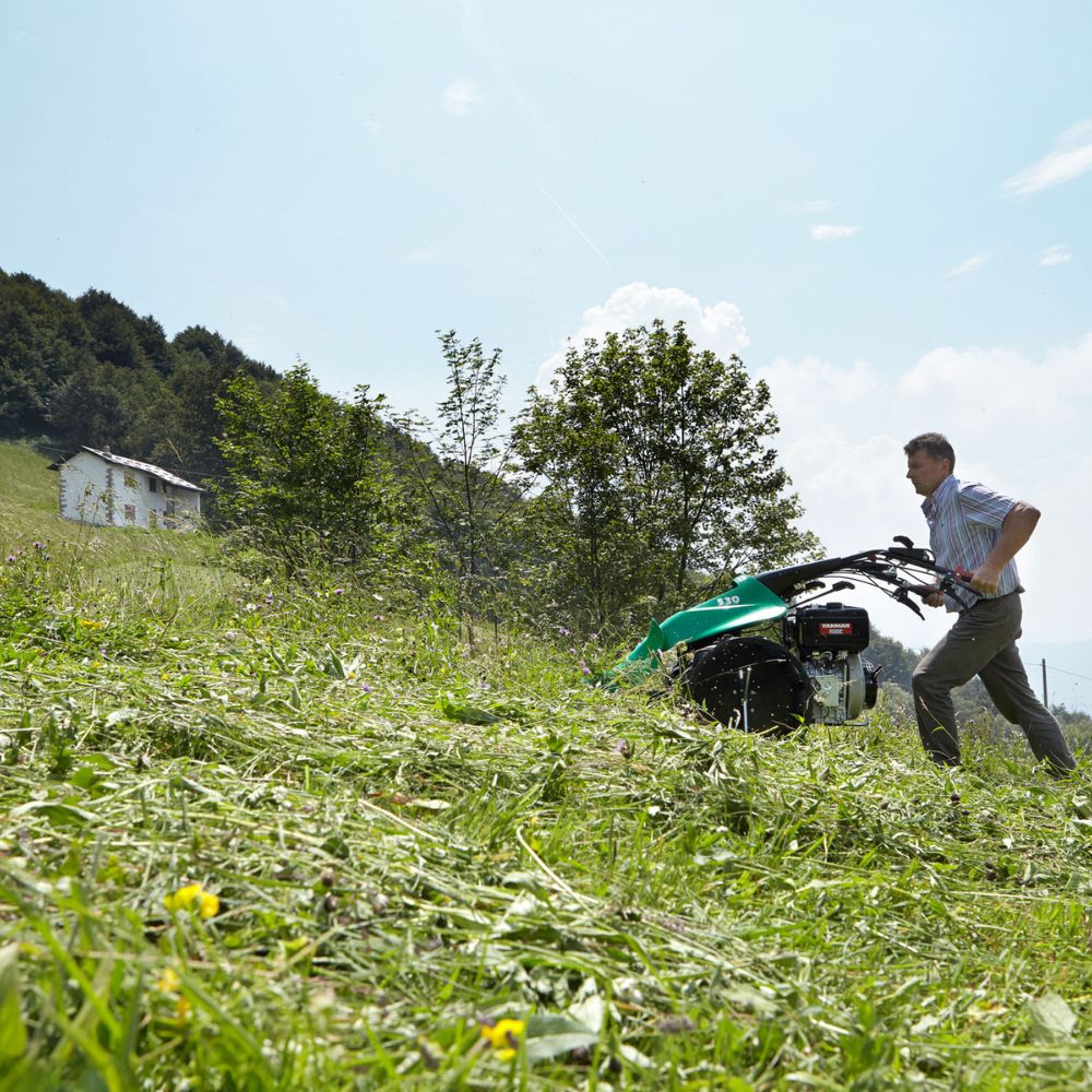Man använder Ferrari 506 PowerSafe på en sluttande äng. Visar slåtterbalkens effektivitet på svår terräng.